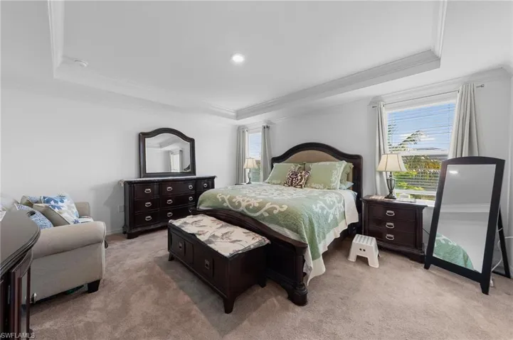 Bedroom with a raised ceiling, light colored carpet, and ornamental molding