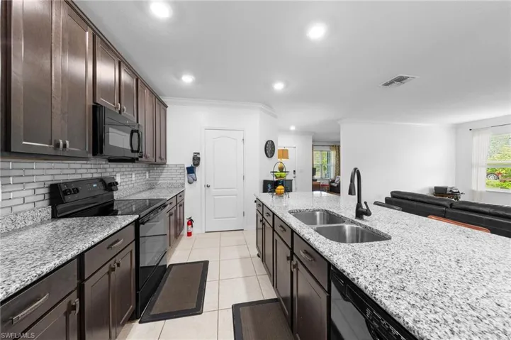 Kitchen featuring black appliances, a sink, dark brown cabinets, decorative backsplash, and light stone counters
