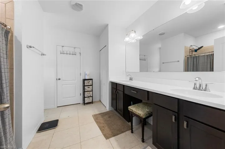 Bathroom with double vanity, tile patterned floors, a tile shower, and baseboards