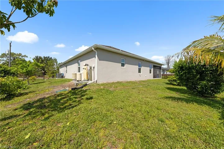 Rear view of house featuring stucco siding, a lawn, and central AC unit