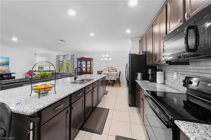 Kitchen featuring black appliances, a sink, decorative backsplash, dark brown cabinetry, and a center island with sink