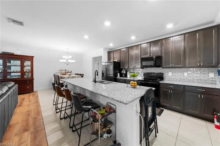 Kitchen featuring black appliances, ornamental molding, a kitchen bar, a sink, and a chandelier
