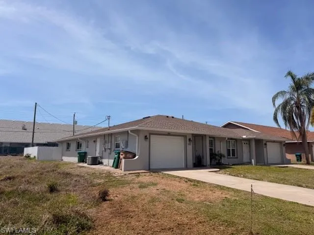 Well-maintained duplex with light gray stucco exterior, white garage doors, and separate driveways offering each unit full privacy