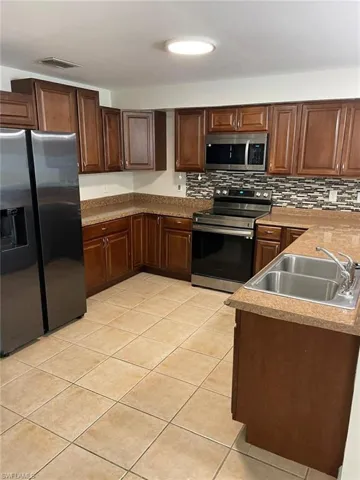 Updated kitchen with rich wood-tone cabinetry, stainless steel appliances, decorative tile backsplash, and tile flooring — move-in ready