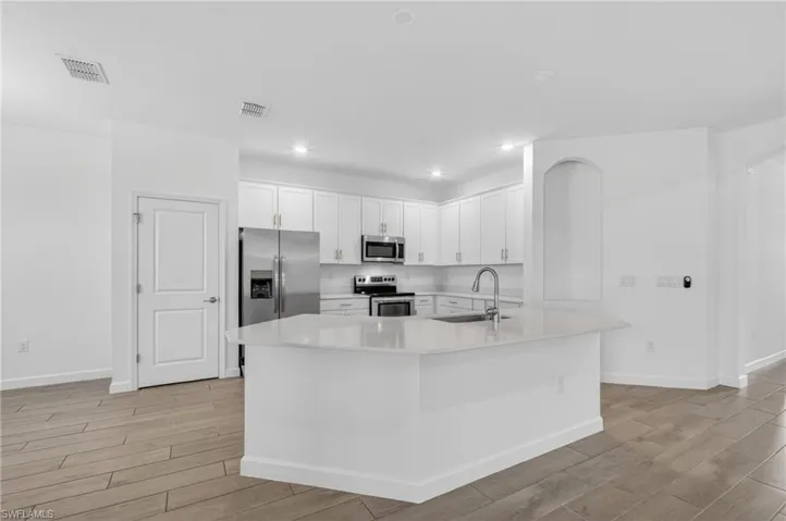 Modern kitchen featuring white cabinetry, stainless steel appliances, a center island with a sink, quartz countertops, and wood-finish tile flooring