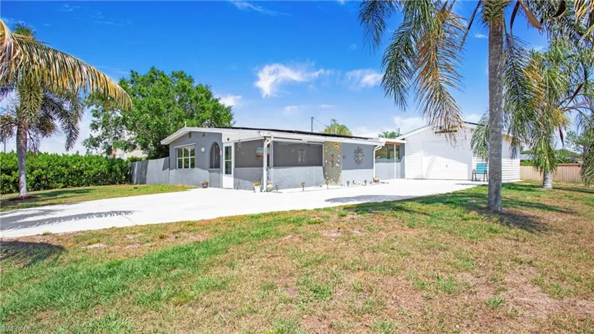 View of front of house with a sunroom, stucco siding, fence, driveway, and a front lawn