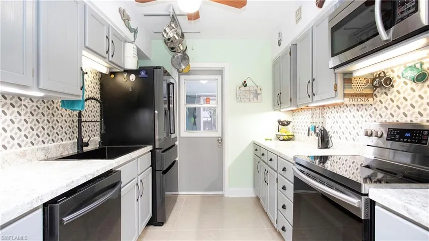 Kitchen featuring light tile patterned flooring, backsplash, a ceiling fan, stainless steel appliances, and baseboards