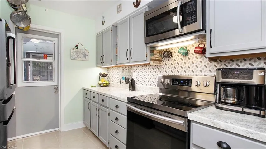 Kitchen featuring light stone counters, light tile patterned floors, baseboards, stainless steel appliances, and decorative backsplash