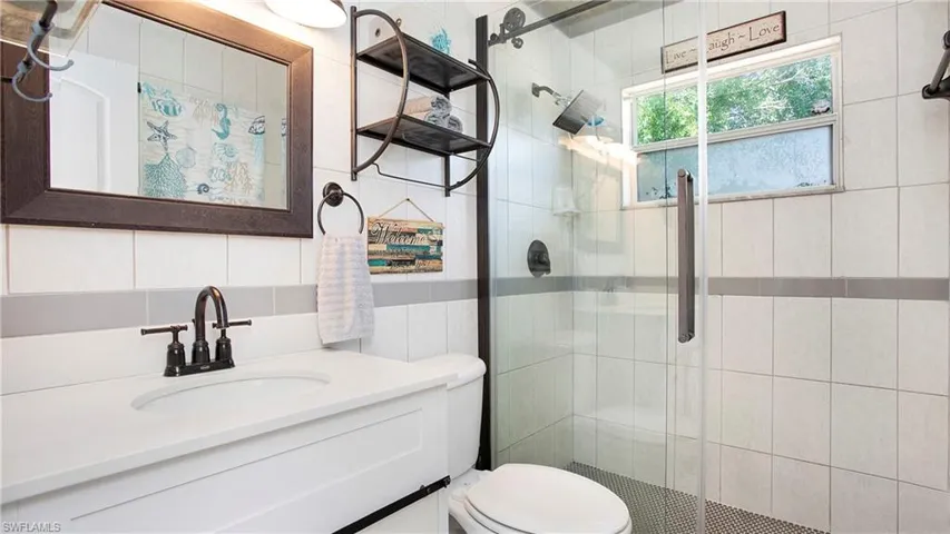 Full bathroom with tile walls, a shower stall, toilet, vanity, and tasteful backsplash