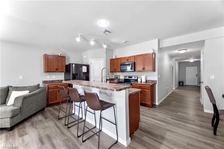Kitchen with appliances with stainless steel finishes, rail lighting, hardwood / wood-style floors, and a kitchen island with sink
