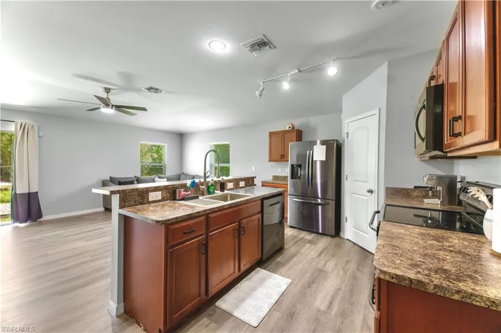 Kitchen with appliances with stainless steel finishes, light hardwood / wood-style flooring, sink, an island with sink, and ceiling fan