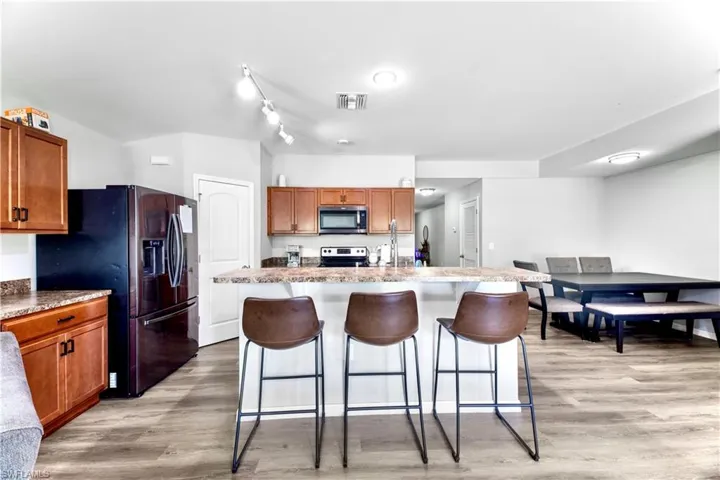 Kitchen featuring rail lighting, light wood-type flooring, a kitchen island with sink, appliances with stainless steel finishes, and a kitchen breakfast bar