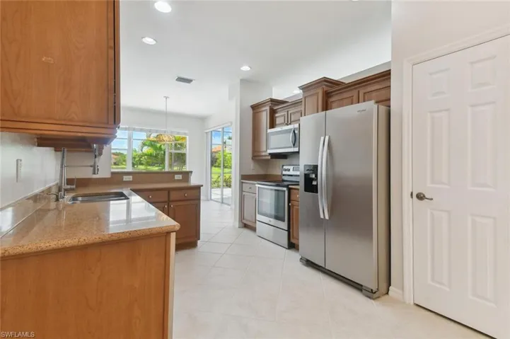 Kitchen with appliances with stainless steel finishes, sink, light stone counters, decorative light fixtures, and light tile patterned flooring