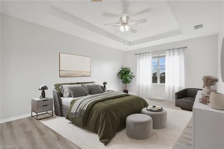Bedroom with ceiling fan, light hardwood / wood-style floors, and a tray ceiling