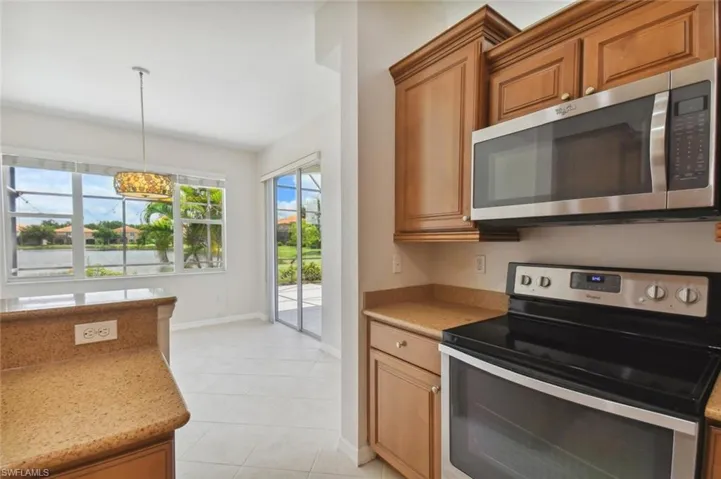 Kitchen with appliances with stainless steel finishes, decorative light fixtures, light tile patterned floors, and light stone counters