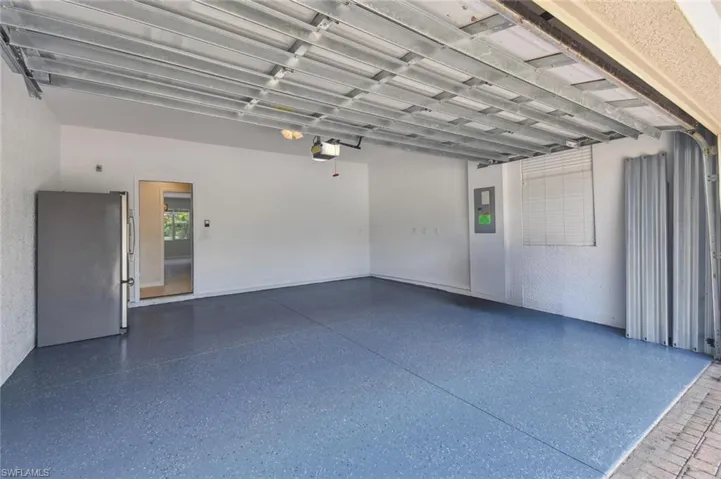 Garage with a garage door opener, stainless steel refrigerator, and electric panel