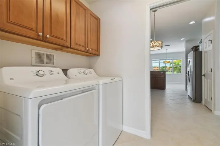 Clothes washing area featuring light tile patterned flooring, washing machine and dryer, and cabinets