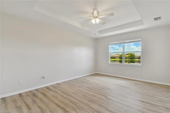 Unfurnished room featuring ceiling fan, a tray ceiling, and light hardwood / wood-style floors