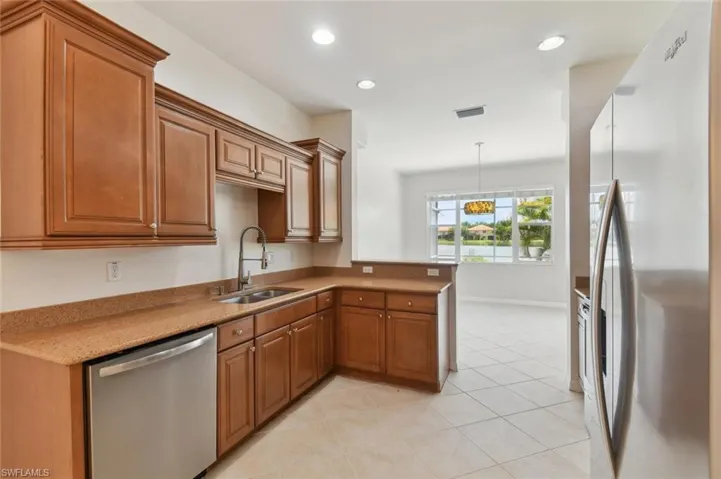 Kitchen with light tile patterned floors, kitchen peninsula, hanging light fixtures, appliances with stainless steel finishes, and sink