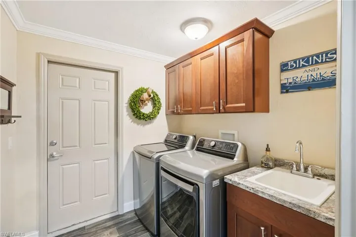 Laundry area with washing machine and clothes dryer, cabinet space, crown molding, and dark wood finished floors