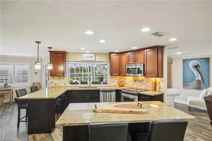 Kitchen featuring light stone counters, crown molding, stainless steel appliances, a kitchen bar, and wood finished floors