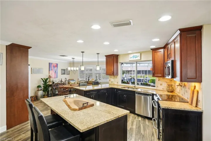 Kitchen with a peninsula, light stone countertops, stainless steel appliances, light wood-style flooring, and ornamental molding