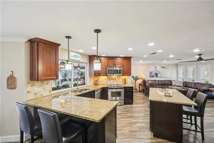 Kitchen with stainless steel appliances, a breakfast bar, light wood-style flooring, decorative backsplash, and recessed lighting