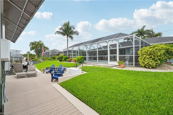 View of grassy yard featuring an outdoor pool, a lanai, and a wooden deck