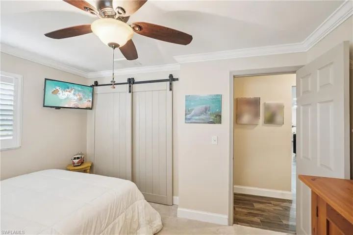 Bedroom with crown molding, a barn door, a ceiling fan, and wood finished floors