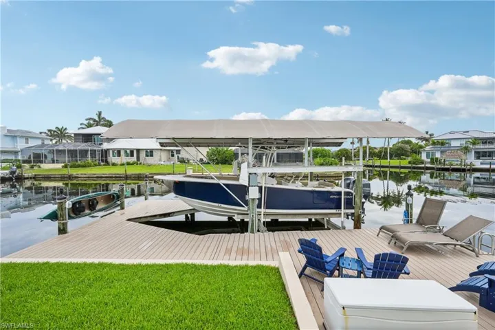 Dock area with boat lift, a water view, a residential view, and a lawn