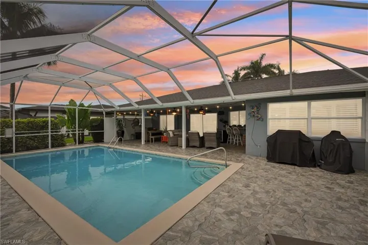 Pool at dusk with an outdoor pool, a patio, area for grilling, and glass enclosure