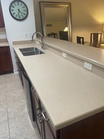 Kitchen with dark brown cabinets, light tile patterned flooring, light stone counters, dishwasher, and a peninsula
