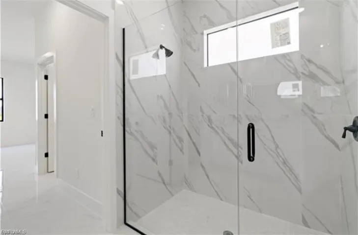 Walk-in shower featuring clear glass enclosure with matte black trim, large-format marble-look wall tiling, and a matte black shower head