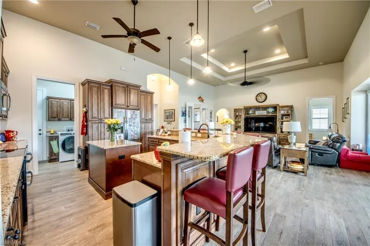 Kitchen featuring ceiling fan, light stone countertops, open floor plan, light wood-style floors, and a raised ceiling