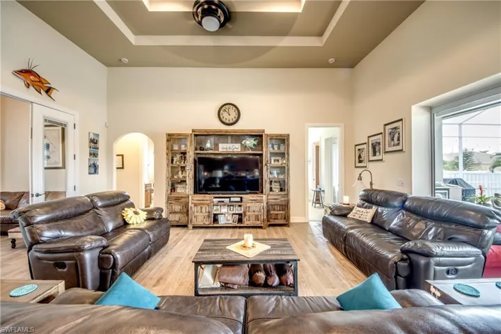 Living room with a high tray ceiling, light wood-style floors, and arched walkways
