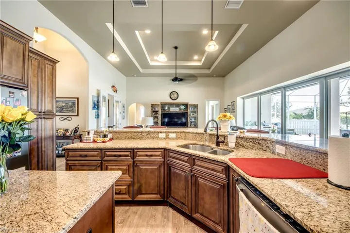 Kitchen featuring arched walkways, light stone counters, a raised ceiling, ceiling fan, and light wood-style floors