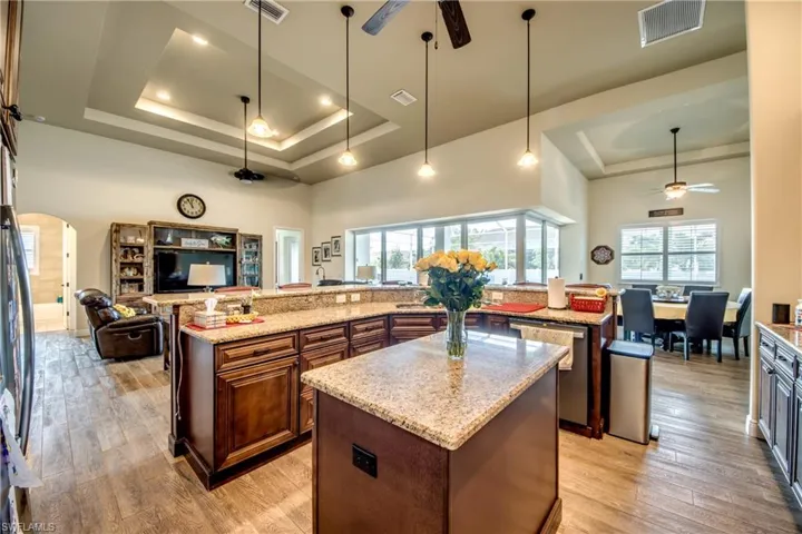 Kitchen featuring ceiling fan, arched walkways, open floor plan, light wood-style floors, and a high tray ceiling