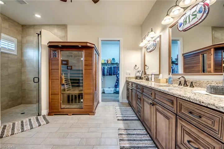 Bathroom with a sauna / steam room, double vanity, a shower stall, a spacious closet, and ceiling fan