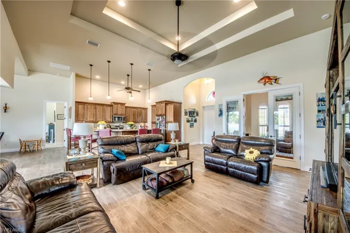 Living area with arched walkways, ceiling fan, a high tray ceiling, light wood-style floors, and recessed lighting