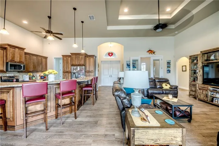 Living area with ceiling fan, arched walkways, a high tray ceiling, recessed lighting, and light wood-style floors