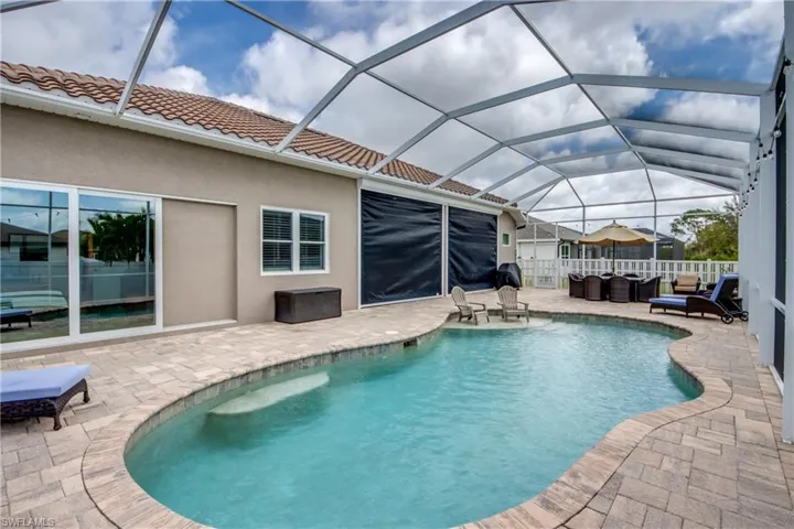 View of pool featuring a sunroom, patio surround, outdoor furniture, and glass enclosure
