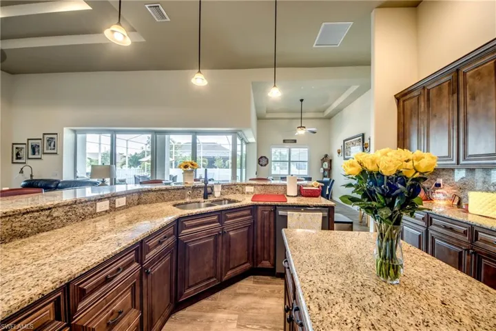 Kitchen featuring a raised ceiling, open floor plan, light stone countertops, dark wood finish cabinets, and light wood-style flooring