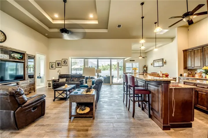 Living room with a ceiling fan, light wood finished floors, and a high tray ceiling