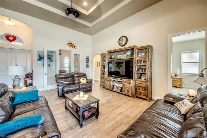 Living area with arched walkways, wood tiled floors, a high tray ceiling, and a ceiling fan