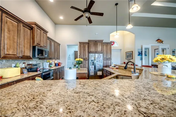 Kitchen with ceiling fan, stainless steel appliances, pendant lighting, light stone counters, and arched walkways