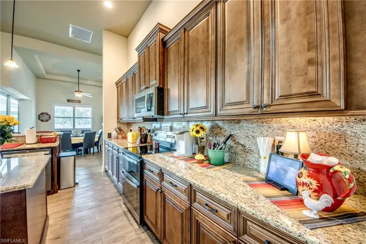 Kitchen featuring stainless steel appliances, light stone countertops, light wood-style floors, decorative backsplash, and decorative light fixtures