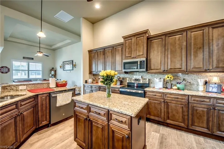 Kitchen featuring ceiling fan, stainless steel appliances, a tray ceiling, light stone counters, and light wood-style flooring