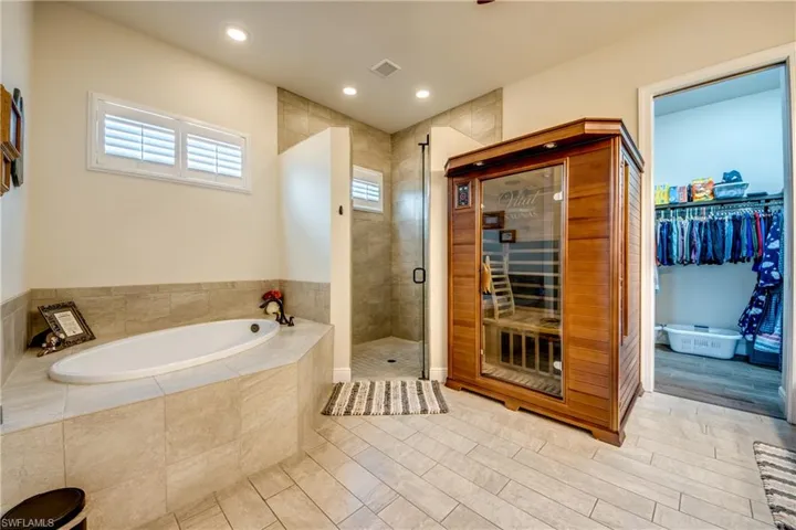Full bath with a sauna / steam room, a spacious closet, a stall shower, a garden tub, and light tile patterned flooring