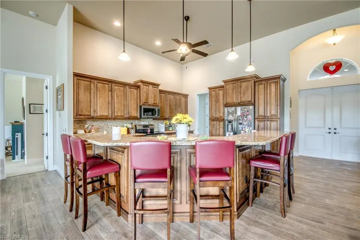 Kitchen with wood finish cabinets, a kitchen breakfast bar, stainless steel appliances, light stone counters, and a high ceiling