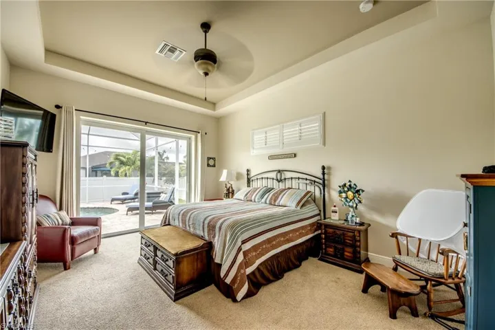 Bedroom featuring a tray ceiling, access to outside, light colored carpet, and a ceiling fan